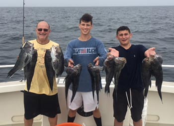 A man and his two sons smile and each hold up four sea bass.