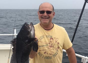 A man smiles and holds up a large sea bass.