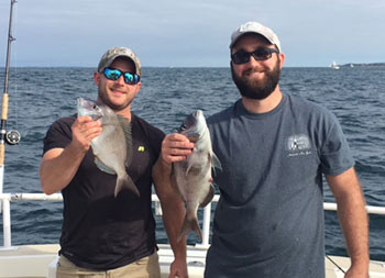 Two men smile and as each hold up a bluefish they caught.