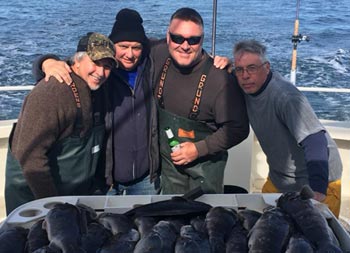 Four men gathered together for a photo stand behind a fillet table full of tautog.