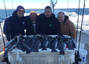 A group of 4 men outfitted in sweatshirts and hats, stand around the filet table where their catch of blackfish is displayed.