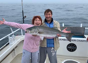 A man and woman proudly smile for the camera and hold up a striped bass.
