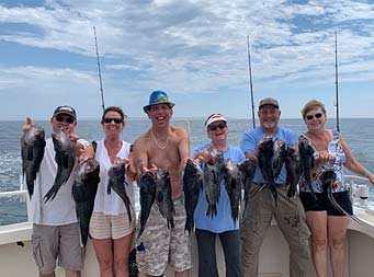 Six men and women smile big for the camera and each hold up the sea bass they caught.