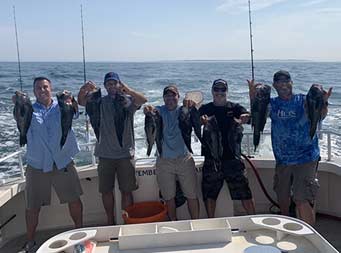 Five men smile as each hold up 2 sea bass.