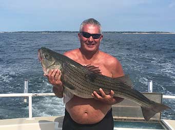 On a clear blue sunny day, a man holds up striped bass and smiles