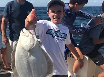 Close up of a young boy holding a fluke with the hook in its mouth.