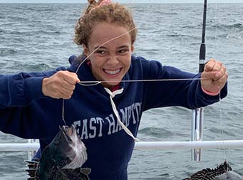 A young woman grins big and holds up her line with the 2 sea bass she caught.