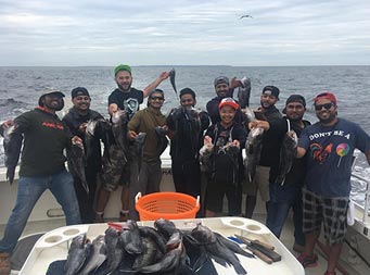 On a partly cloudy day, 10 men stand close together and smile as each hold up 2 sea bass.