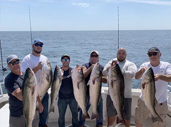 Six men ranging in age, each hold up the striped bass they caught.