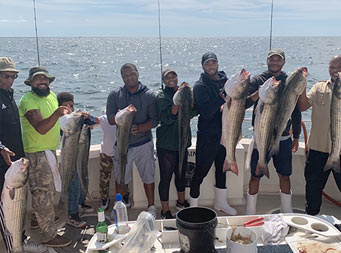Six men, one woman and 2 young  boys stand together for a photo. All of them hold up the striped bass they each caught.