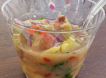 Close up of plastic cup with a colorful ceviche mix of fish, pineapple, onion and other ingredients.