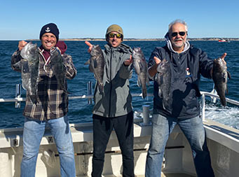Three men on the boat on the water each hold up 2 sea bass and smile.